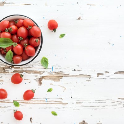 Cherry tomatoes in metal bowl and fresh basil leaves on