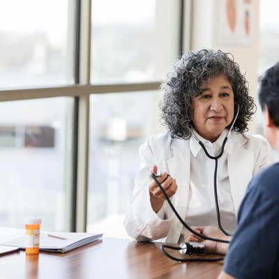 Mature female doctor takes blood pressure of unrecognizable male patient