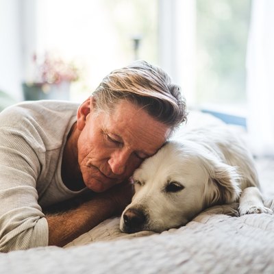 Retired man sleeping with dog comfortably on bed at home