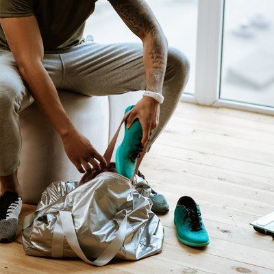 Dark-skinned sportsman with tattoo putting sneakers into bag