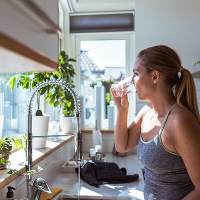 Side view of woman in sports clothing drinking water at kitchen