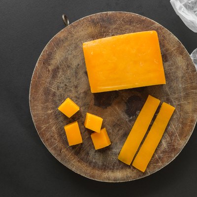 Block, slices and cubes cheddar cheese on a wooden cutting board