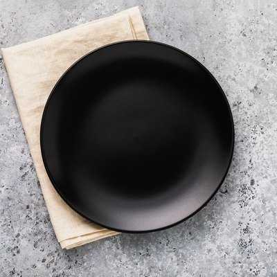 Empty ceramic plate in black with a napkin on a gray concrete table, top view