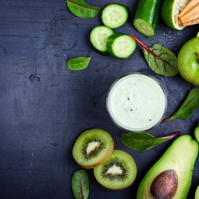 Green smoothie with fruit and vegetable ingredients on grey rustic table with copy space