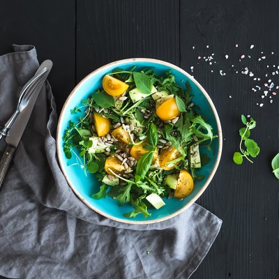 Bowl of green salad with avocado, arugula, cherry tomatoes and sunflower seeds