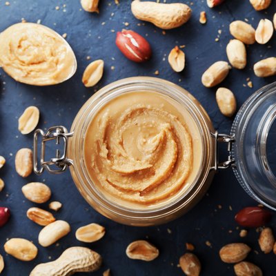 Peanut butter jar and heap of nuts on vintage table top view.