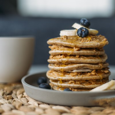 Side view of a stack of homemade pancakes on a plate, topped with blueberries and bananas