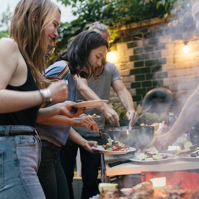 A Group Of Friends Helping Themselves To Food At A Summer Barbecue