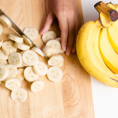 Cropped Hands Cutting Banana On Chopping Board