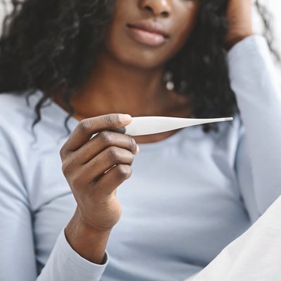 Sick woman with fever checking her temperature in bed