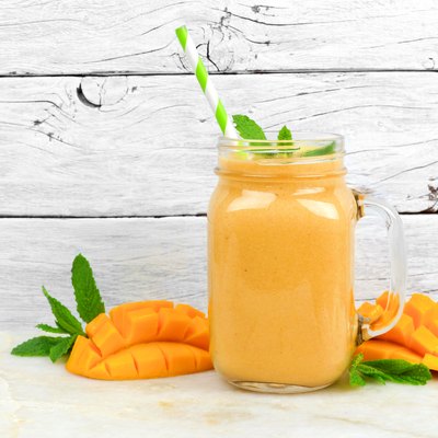 Mango coconut smoothie in a mason jar, on rustic white wood