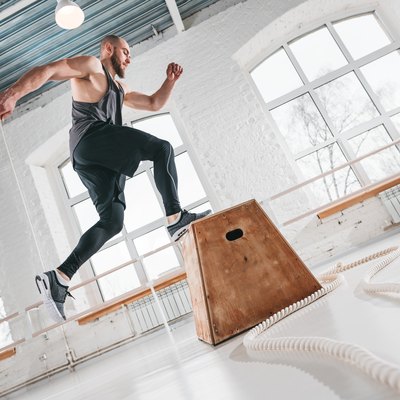 Strong man doing a box jump exercise at workout gym. Male athlete using box for gym exercises