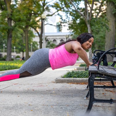 woman doing incline push-ups outdoors on a bench as part of a full-body workout