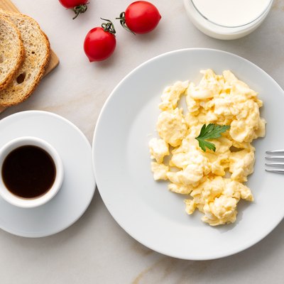 Breakfast with pan-fried scrambled eggs, cup of coffee, tomatoes on white stone background. Omelette, top view