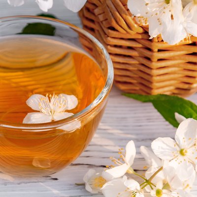 Basket with Flowers of philadelphus somewhere called jasmine or mock orange and Cup with fragrant jasmine tea on a white wooden tray outdoors in summer