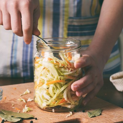 Woman cook sauerkraut or salad on wooden background. Step 5 - Put the cabbage in the jars. Fermented preserved vegetables food concept.