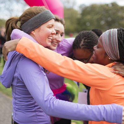 Happy female runners hugging at charity race finish line, celebrating