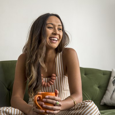 Laughing young woman with coffee mug sitting on couch