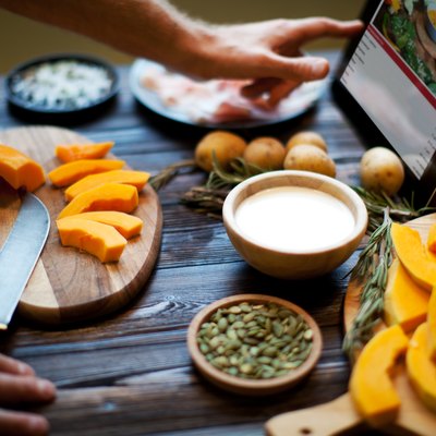 A man's hands cutting up vegetables while reading a recipe from a tablet