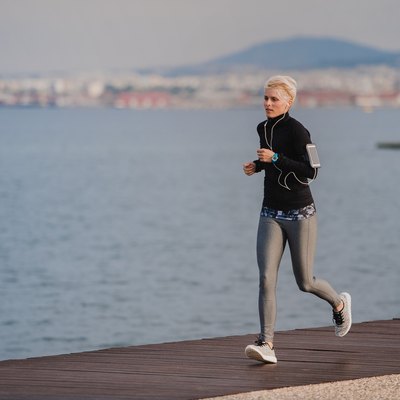 Side view of young sportswoman running outdoors on beach.
