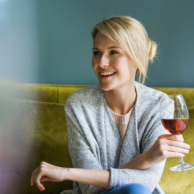 A smiling woman holding a glass of red wine and sitting on a green sofa