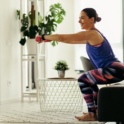 Happy female athlete exercising with dumbbells at home.
