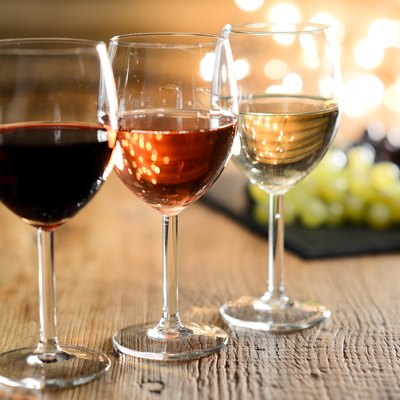 three glass of white red and rose wine with dim light in wooden restaurant table with a grape background