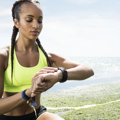 Young woman beside sea, wearing sports clothing, looking at activity tracker