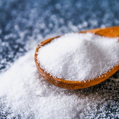 Crystals of shallow salt in a scoop, spoon on a dark gray table. Background for advertising salt. Table salty. Salted food.