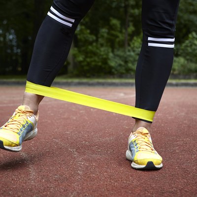 Legs of young woman training in park, stretching resistance band