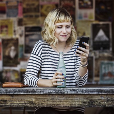 Woman using smart phone while holding soda bottle in cafe