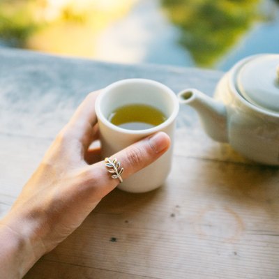Cropped Hand Holding Green Tea Cup By Teapot On Table