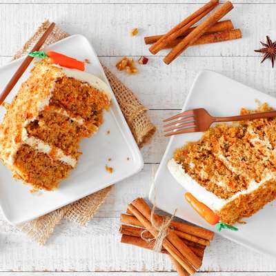 Two slices of homemade carrot cake with cream cheese frosting, top view table scene over white wood