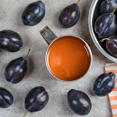 Ripe plums and plum juice in a mug on the table.