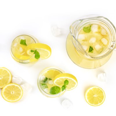 Homemade lemonade in glasses and a jar, with fresh lemons, mint, and ice cubes, shot from the top on a white background with copy space