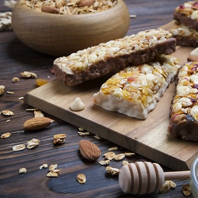 A trail mix bowl of dried fruit, raisins, cranberry with almonds, raisins, seeds, cashew, hazelnut nuts with honey. Vegetarian fitness energy bar snacks. Close up, top side view, background.