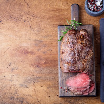 Roast beef on cutting board. Wooden background. Top view. Copy space.