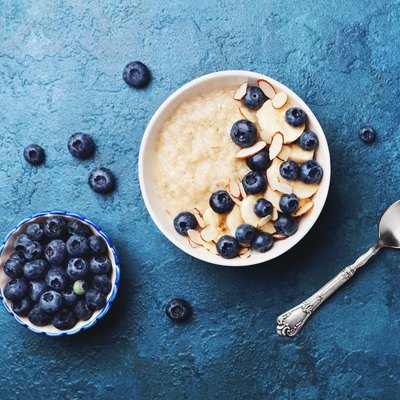 Bowl of oatmeal porridge with banana and blueberry on vintage table top view in flat lay style. Homemade breakfast.