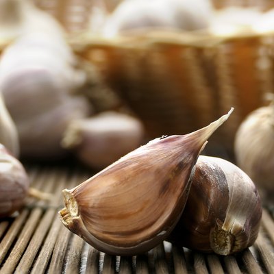 Close-up of garlic cloves in a dark husk. Wicker basket with garlic in the background. Selective focus.