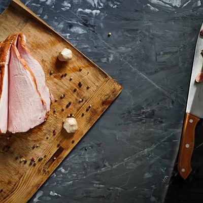 Delicious smoked ham on a wooden board, on a dark concrete background with spices. Top view