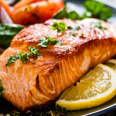 Barbecued protein-rich salmon, fried potatoes, vegetables and lemons on plate