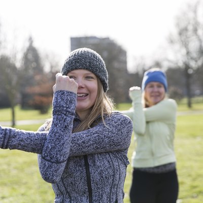 Smiling woman exercising, stretching arm in sunny park