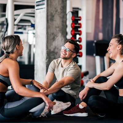 Happy friends sitting on the floor in the gym and talking.