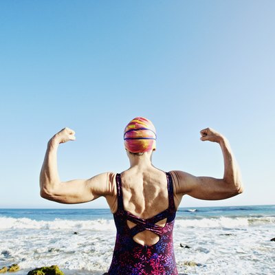 Older Caucasian woman flexing her upper body muscles on beach