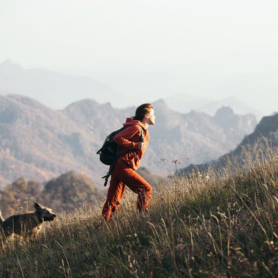 Beautiful woman traveler climbs uphill with a dog on a background of mountain views.