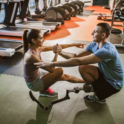 Happy male and his girlfriend cooperating while exercising in a gym.