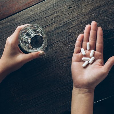 Cropped Hands Of Woman Holding Pills And Drinking Water In Glass