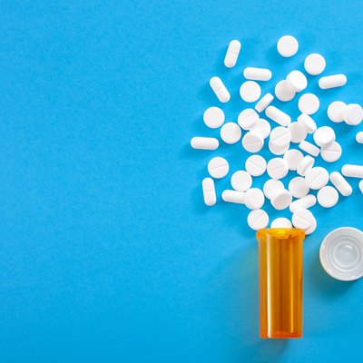 Pills falling from pill bottle on blue background with copyspace