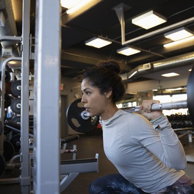 Focused woman doing barbell squats in gym