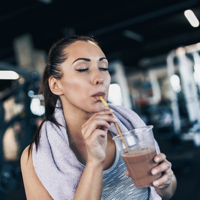 Young woman drinking glass of shake after workout in fitness gym